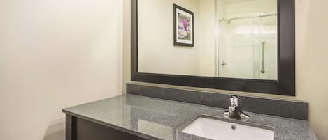 Un baño con encimera de granito, un lavabo blanco y un espejo grande.