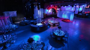 Un espacio interior amplio con varias áreas de comedor, un escenario central con una plataforma circular y un fondo que presenta un gran arco.