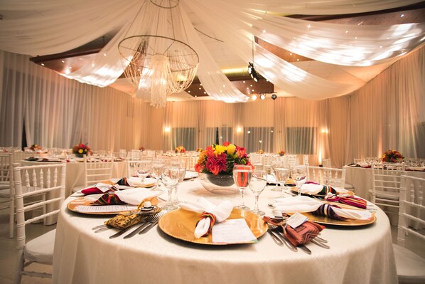 A banquet hall with round tables set for a formal event, featuring white tablecloths, gold chargers, and floral centerpieces.