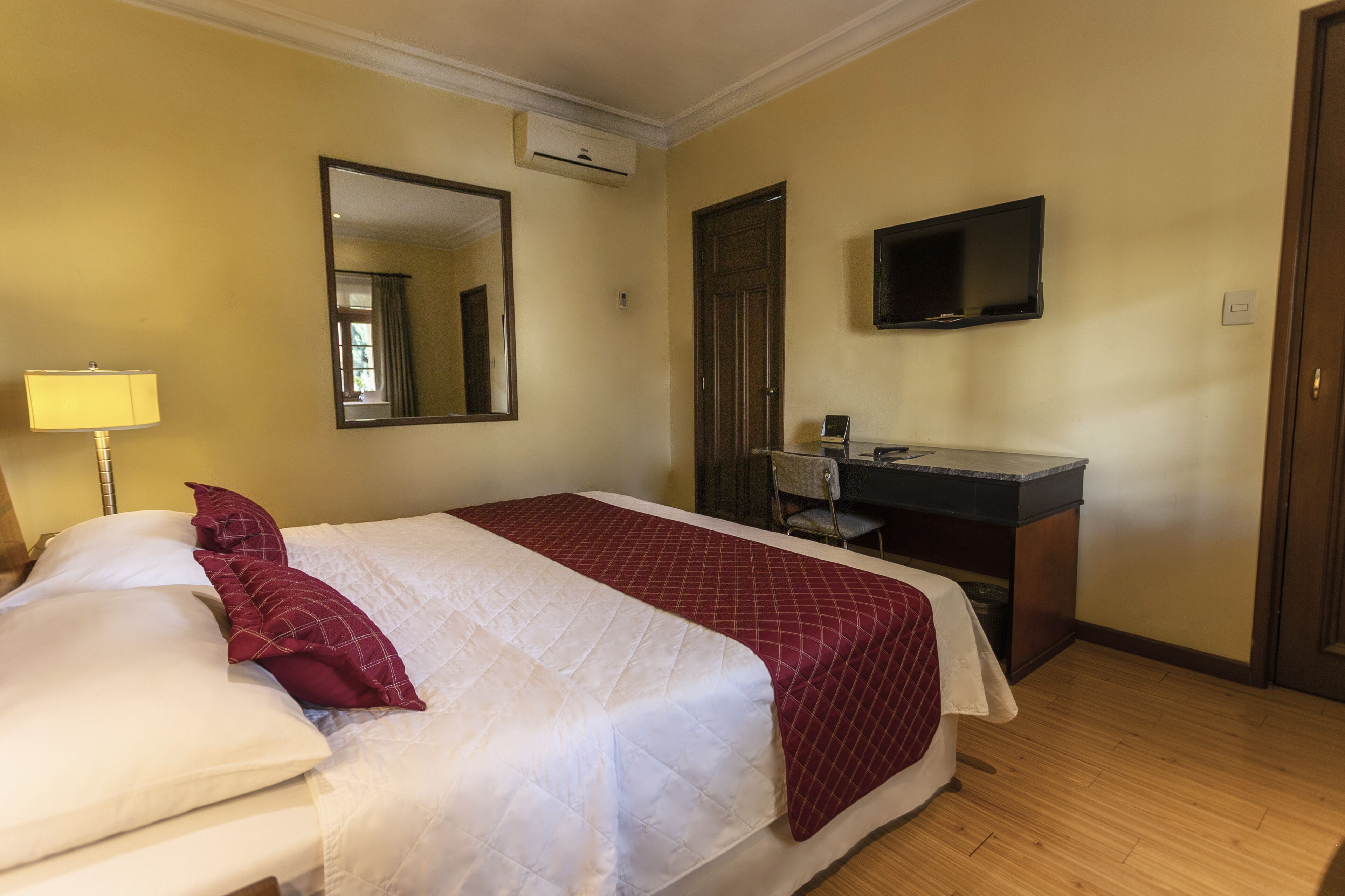 A hotel room with a bed, a desk with a chair, a television, and a mirror.