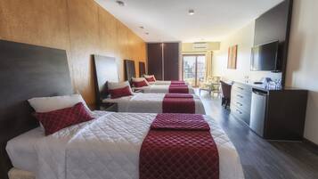 Una habitación de hotel con tres camas, un escritorio, un televisor y un armario.