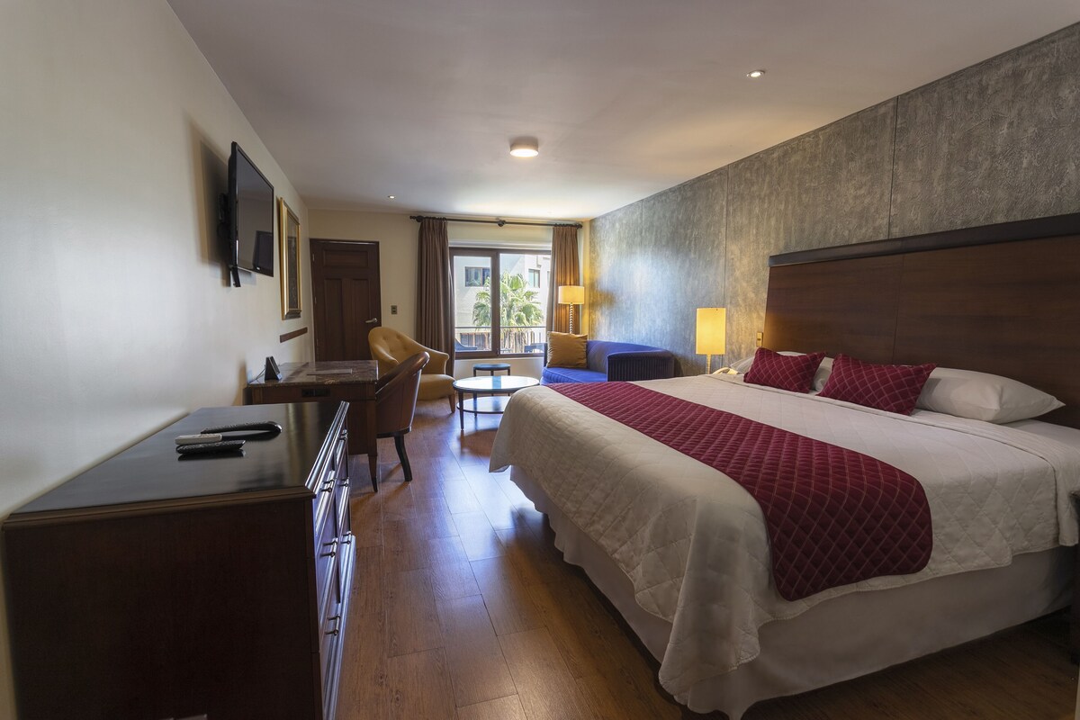 A hotel room with a bed, desk, chair, and a TV mounted on the wall.
