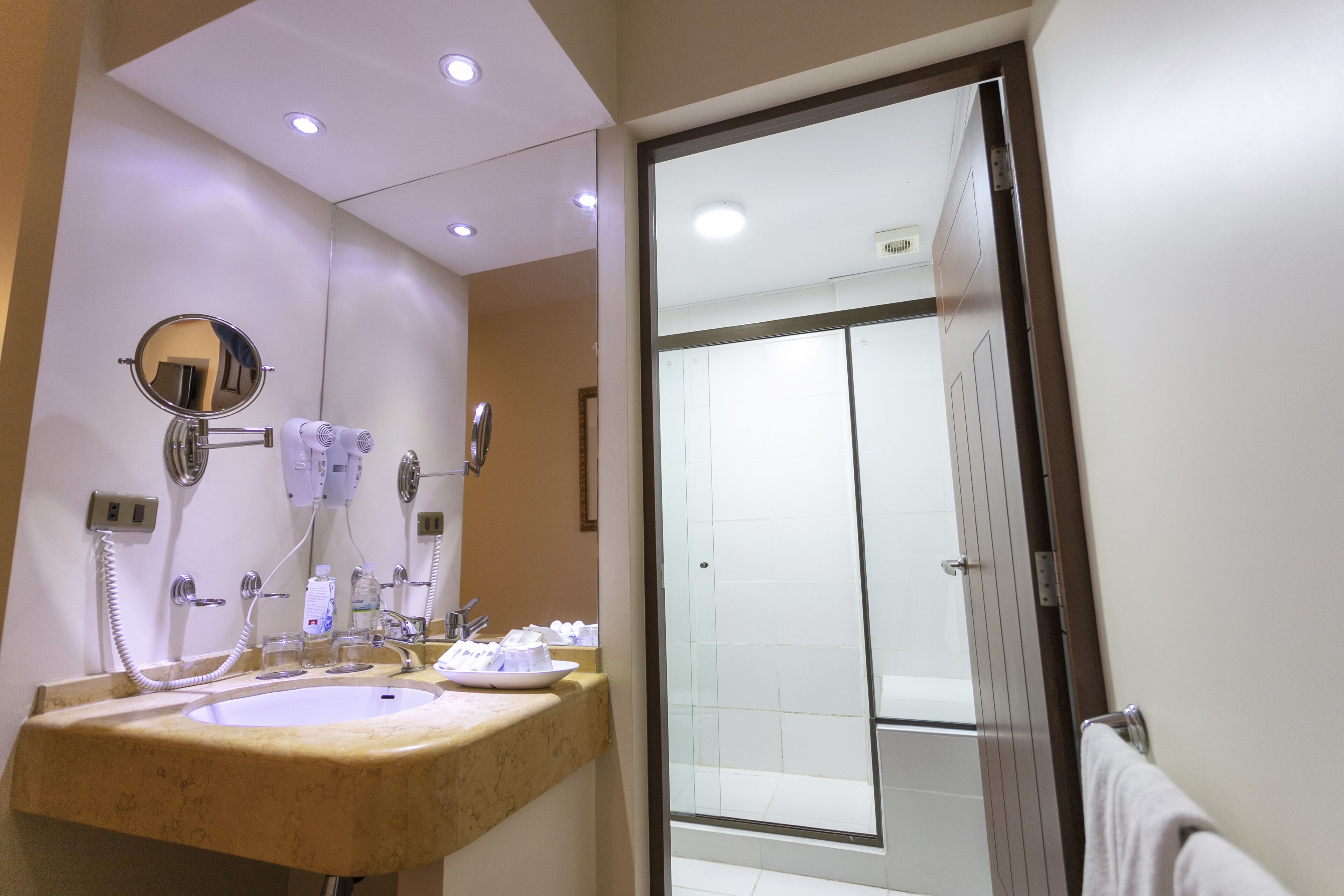 Une salle de bain équipée d’un double lavabo, d’un miroir, d’un sèche-cheveux et d’une cabine de douche en verre.