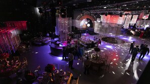 Un espacio amplio con varias mesas dispuestas para comer, un escenario con un gran fondo circular y una cabina para DJ.