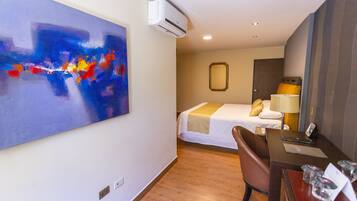 Une chambre d’hôtel avec un lit, un bureau, une chaise et un tableau abstrait au mur.
