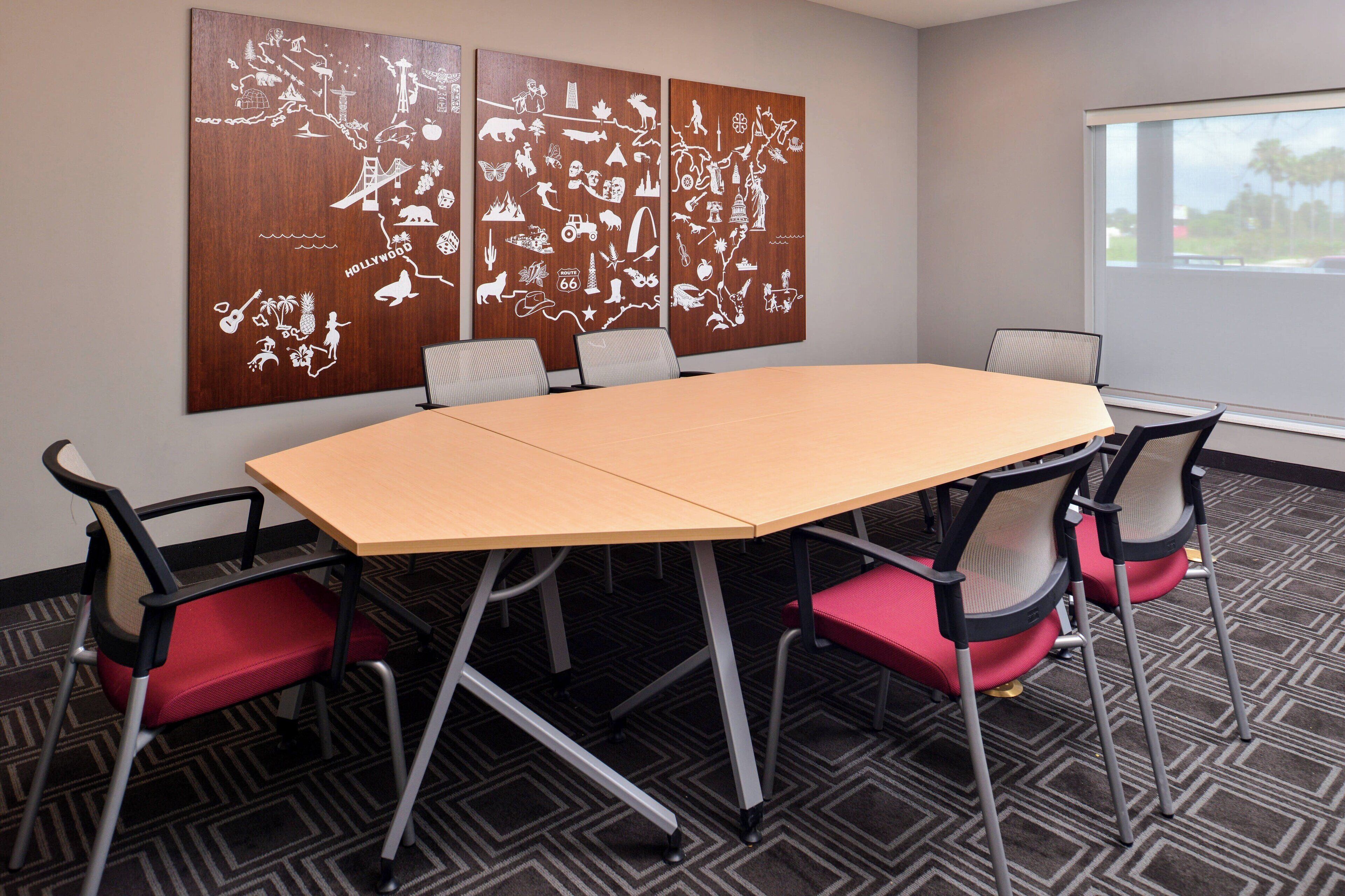 Un salón de conferencias con una mesa grande, seis sillas y un mural de un mapa en la pared.