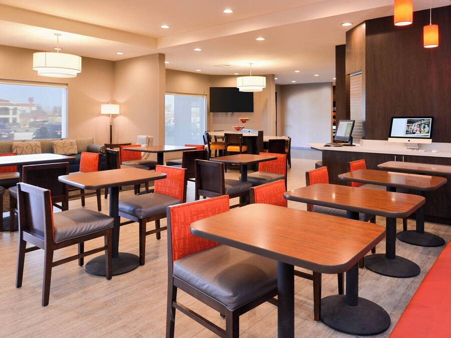 A modern hotel lobby with multiple seating areas, including tables and chairs, a reception desk, and a large TV screen.