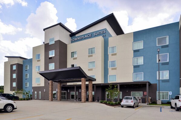 A multi-story hotel with a modern design, featuring a covered entrance and a parking area with several cars.
