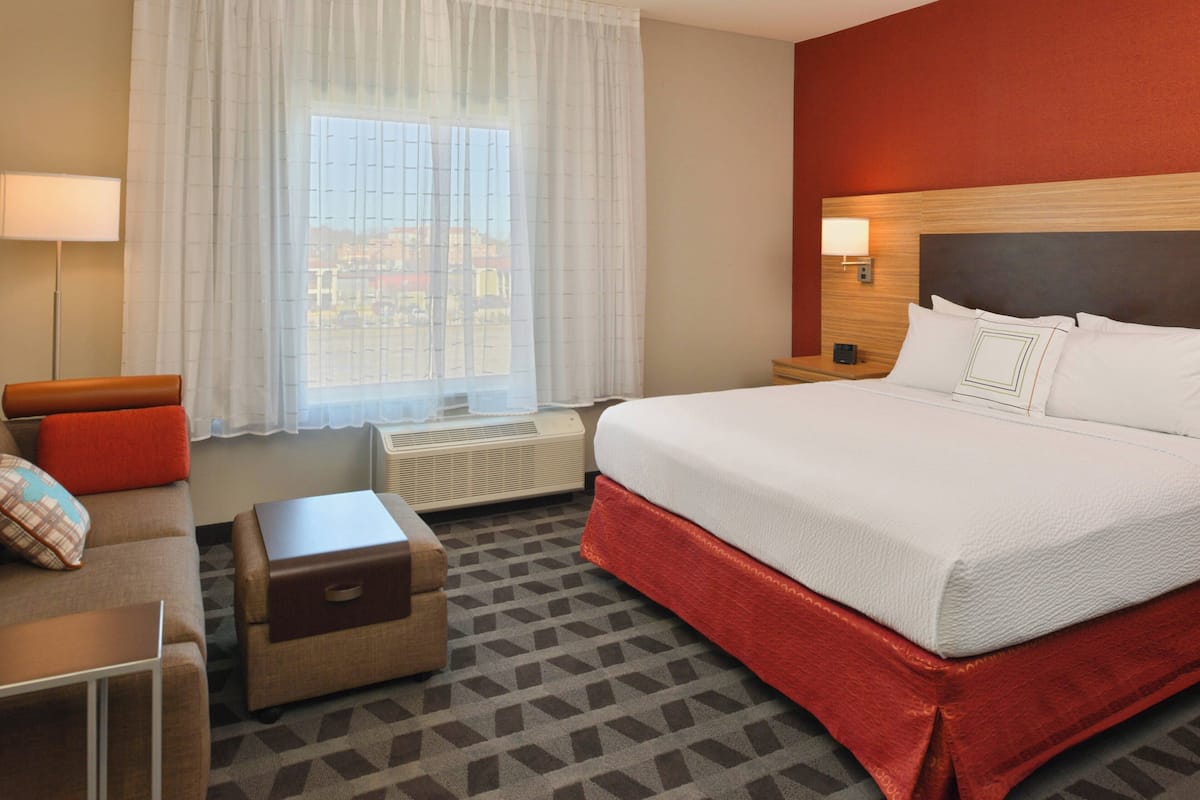 Ein Hotelzimmer mit einem großen Bett, einer Couch, einem kleinen Tisch, einem Nachttisch und einem Fenster mit Vorhängen.