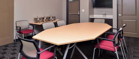A conference room with a large table, four chairs, a television, and a kitchenette area.