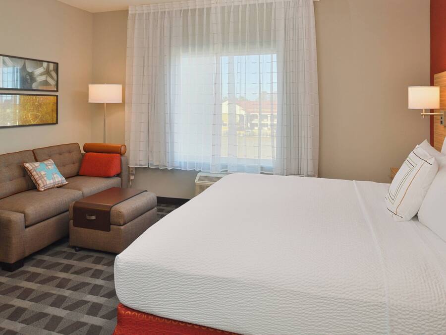 A hotel room with a large bed, a sofa, a small table, and a window with curtains.