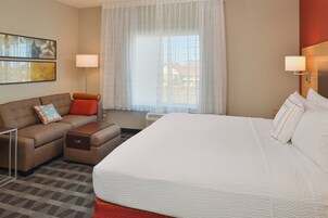 Una habitación de hotel con una cama grande, un sofá, una mesita y una ventana con cortinas.