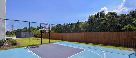 An outdoor basketball court with a chain-link fence, a basketball hoop, and a wooden fence in the background.