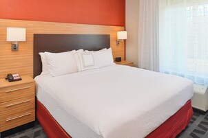 Una habitación de hotel con una cama grande, dos mesitas de noche, un teléfono y una ventana con cortinas.