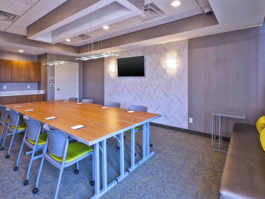 A conference room with a long table, chairs, a sofa, and a TV on the wall.