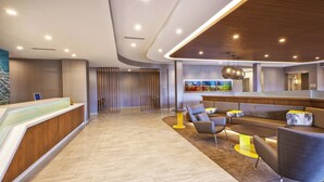 A modern reception area with a wooden reception desk, seating area with chairs and a sofa, and a large abstract painting on the wall. - SpringHill Suites by Marriott St. Joseph Benton Harbor (Benton Harbor)