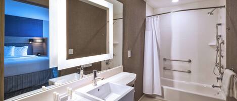 Un baño de hotel moderno con un espejo grande, lavamanos dobles, una bañera y una ducha.