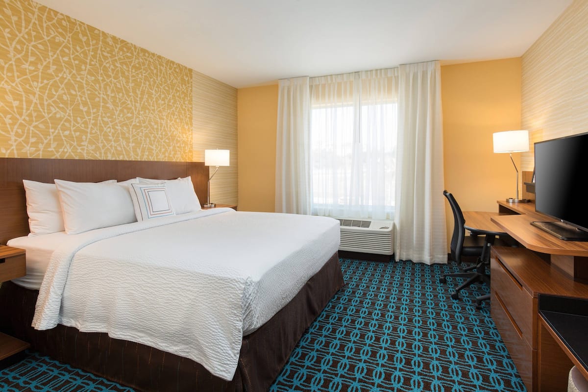 Een hotelkamer met een groot bed, een bureau met een computer, een televisie en een raam met gordijnen.