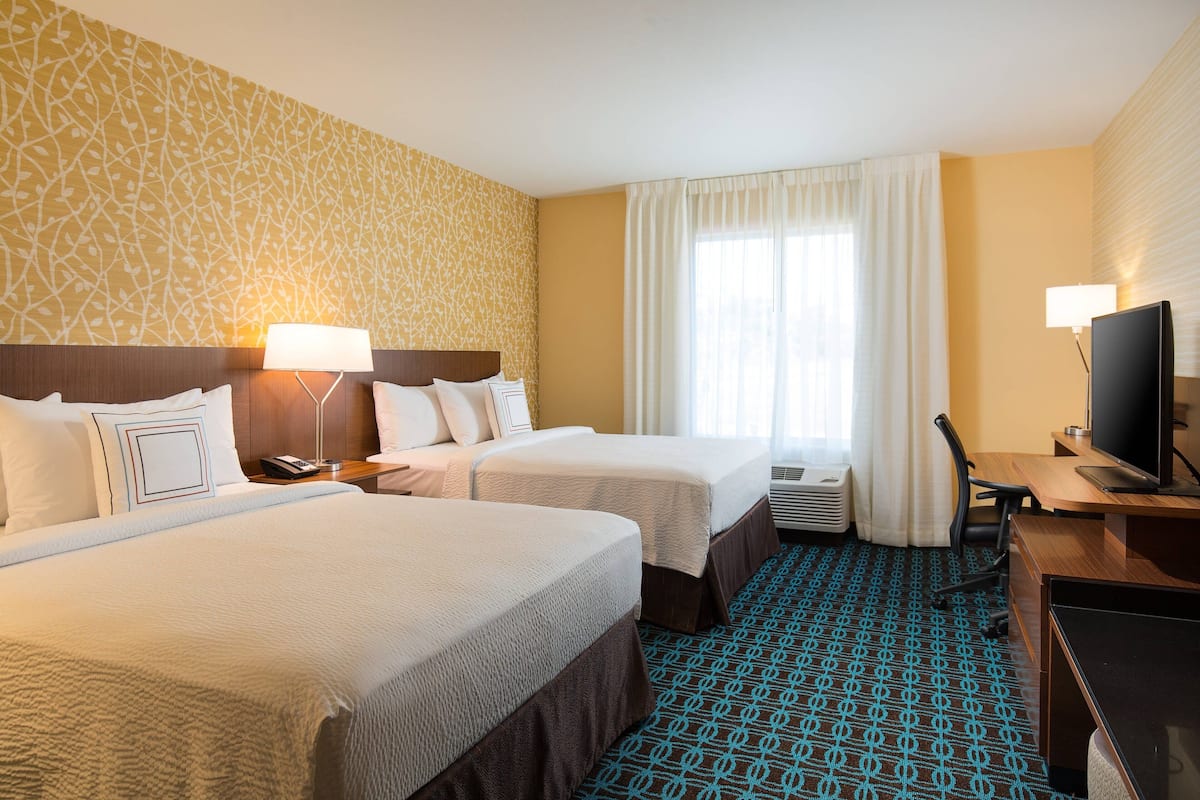 Een hotelkamer met twee bedden, een bureau, een televisie en een kamerbreed tapijt met een patroon.
