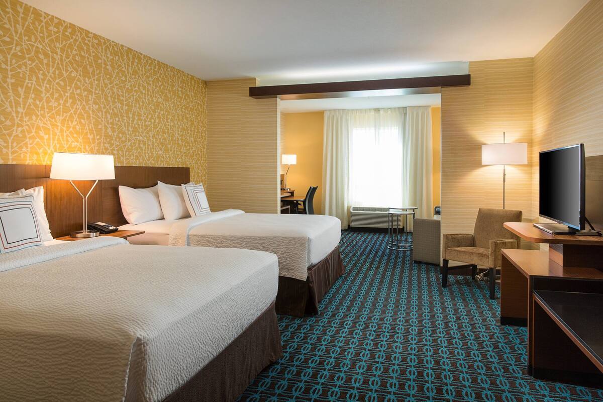 Een hotelkamer met twee bedden, een bureau met een televisie en een zithoekje.