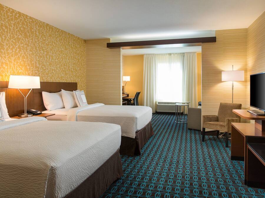 A hotel room with two beds, a desk with a TV, and a small seating area.