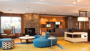 Een moderne hotellobby met een blauwe bank, een open haard, een receptiebalie en een groot raam met gordijnen.