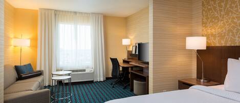 Ein Hotelzimmer mit Bett, Schreibtisch, Stuhl, Nachttisch und Fernseher.