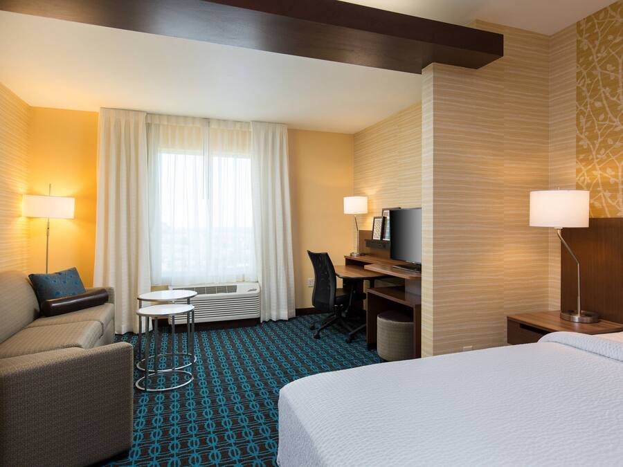 A hotel room with a bed, a desk, a chair, a small table, and a TV.