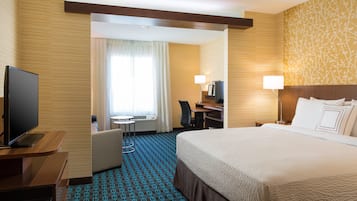 A hotel room with a large bed, a desk with a computer, a TV, and a chair.