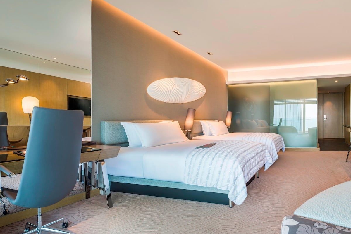 A modern hotel room with a large bed, a desk, a chair, and a TV.