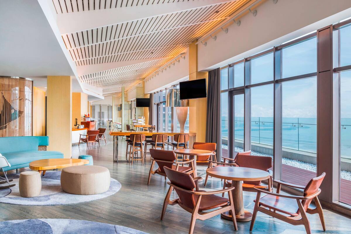 A modern lounge area with round tables and chairs, a blue sofa, and a large window offering a view of the sea.