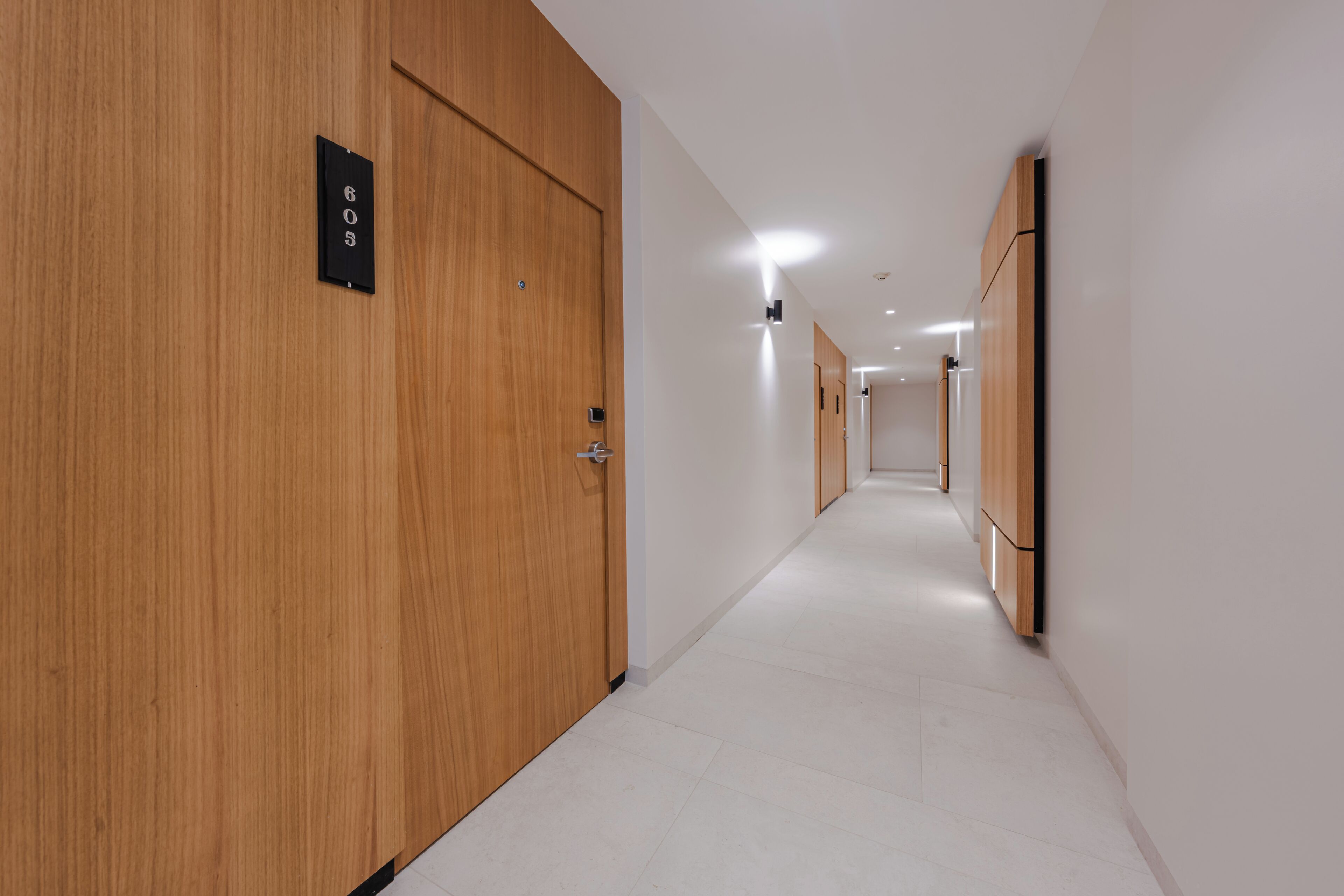 A modern hotel corridor with wooden doors, a sign indicating room number 605, and a clean, tiled floor.