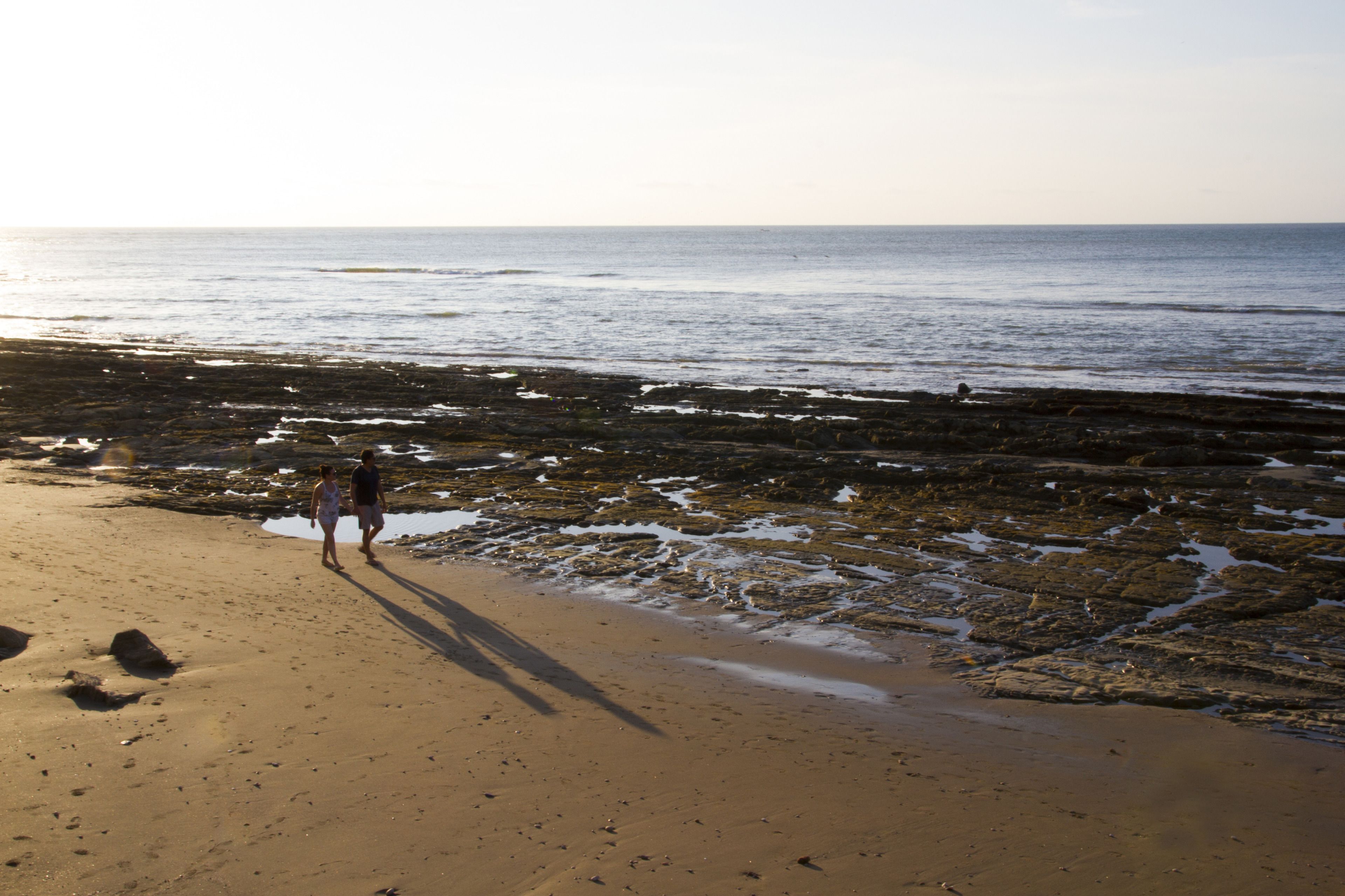 Une plage avec un terrain rocheux, et une personne qui marche.
