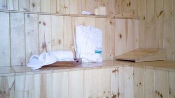 Ein Holzsaunaraum mit Bänken, Handtüchern und einem Holzregal mit persönlichen Gegenständen.