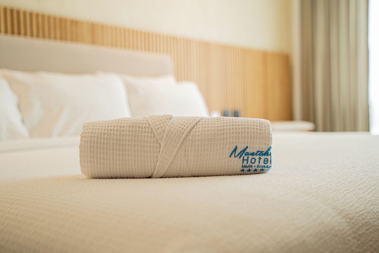 Una bata ordenada doblada sobre una cama, con el logotipo y el nombre del hotel a la vista.
