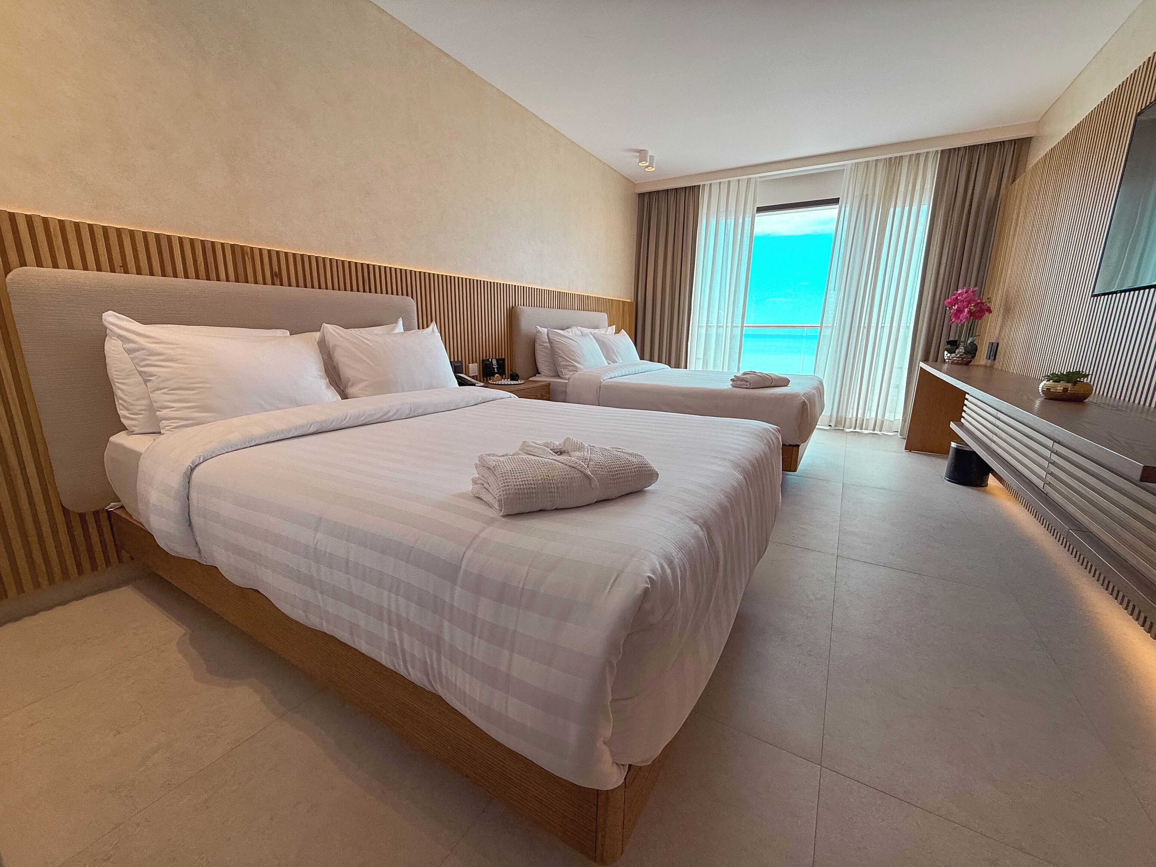 Ein Hotelzimmer mit einem großen Bett, einem kleineren Bett, einem Schreibtisch und Meerblick.