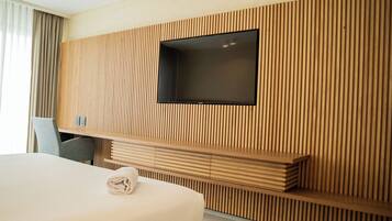 A modern hotel room with a large bed, a flat-screen TV mounted on a wooden slat wall, and a seating area with a bench.