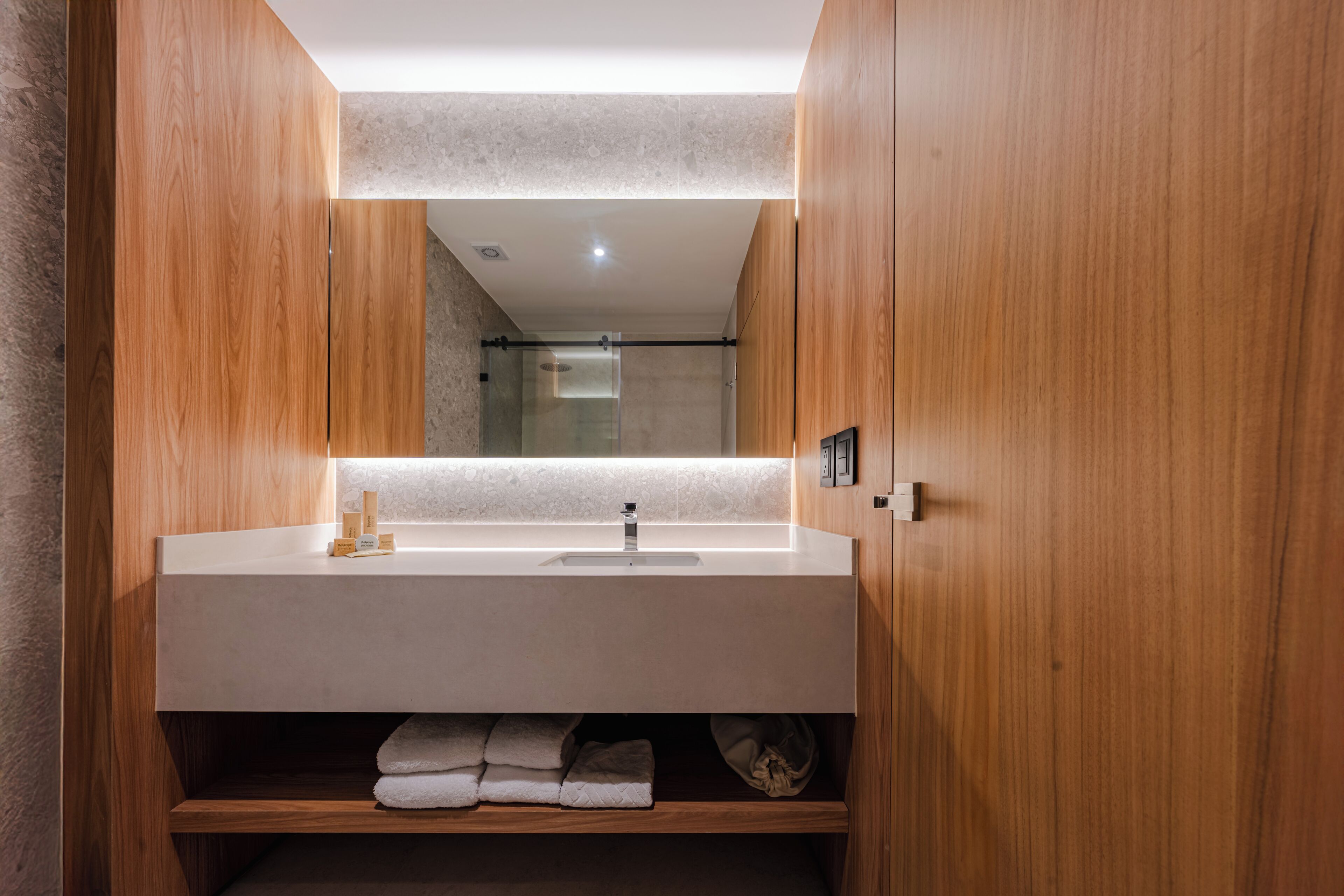 Une salle de bain moderne avec un meuble-lavabo en bois, un grand miroir et une cabine de douche intégrée.
