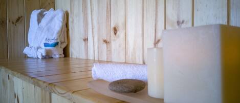 A wooden spa area with a towel, a candle, and a stone on a shelf.
