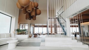 A spacious lobby with a modern staircase, white sofas, and hanging wooden light fixtures.
