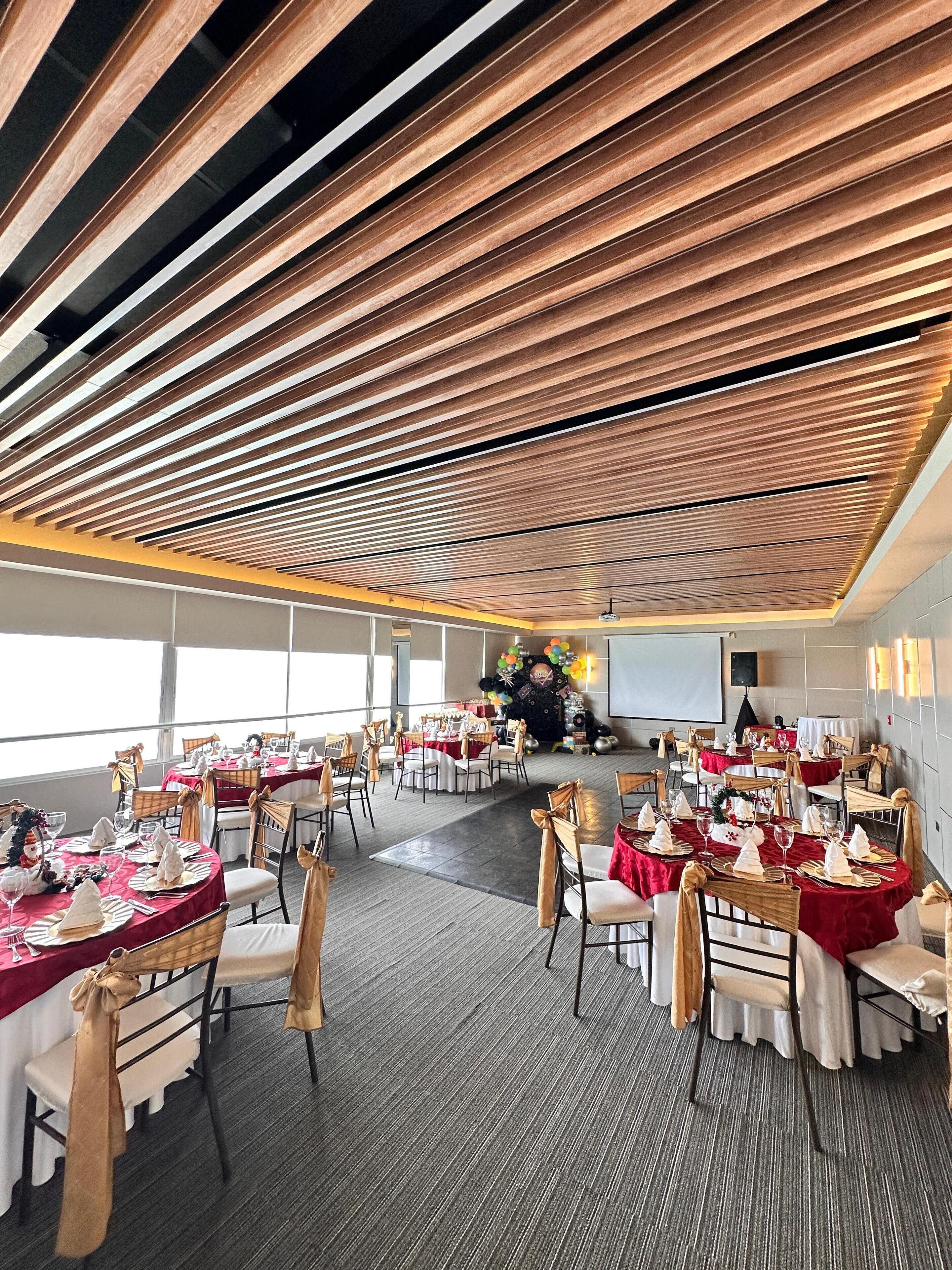 A spacious banquet hall with tiered wooden ceilings and multiple round tables set for a formal event.
