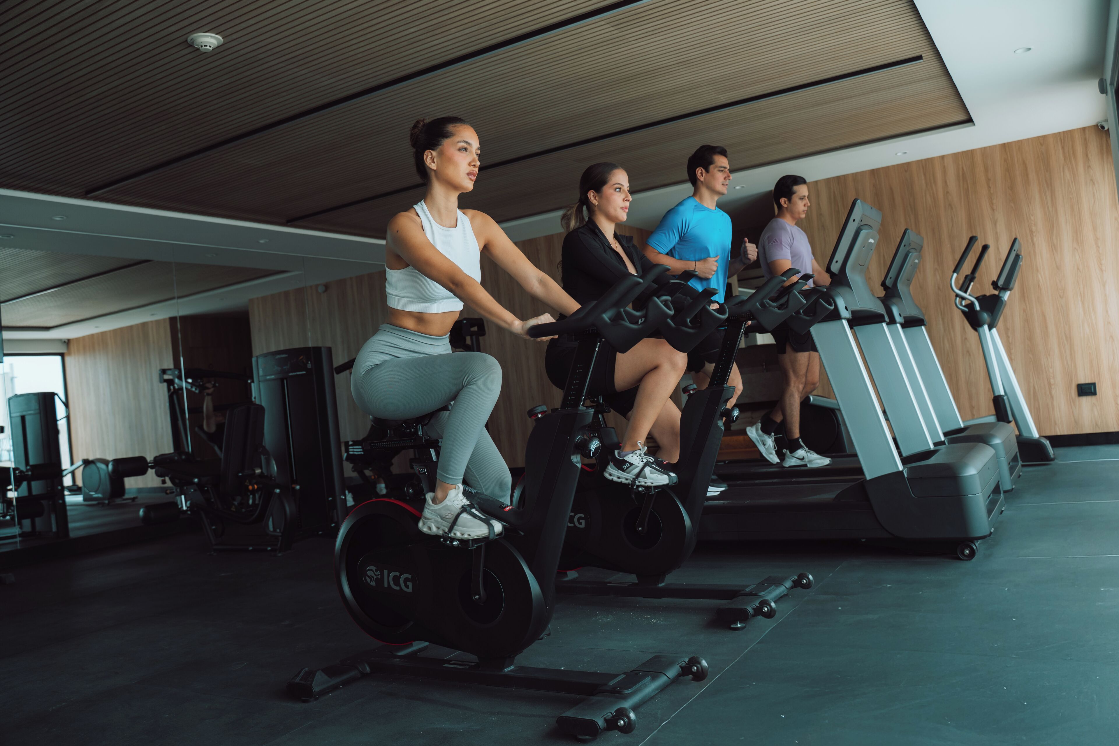 Een sportschool met hometrainers en loopbanden, houten wanden en fitnessapparatuur.