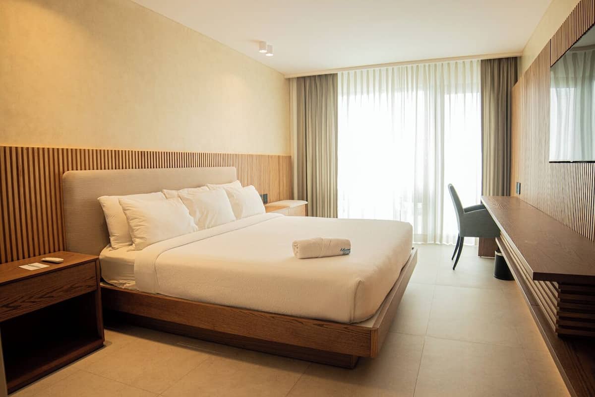 A modern hotel room with a large bed, a wooden headboard, a desk, and a TV.