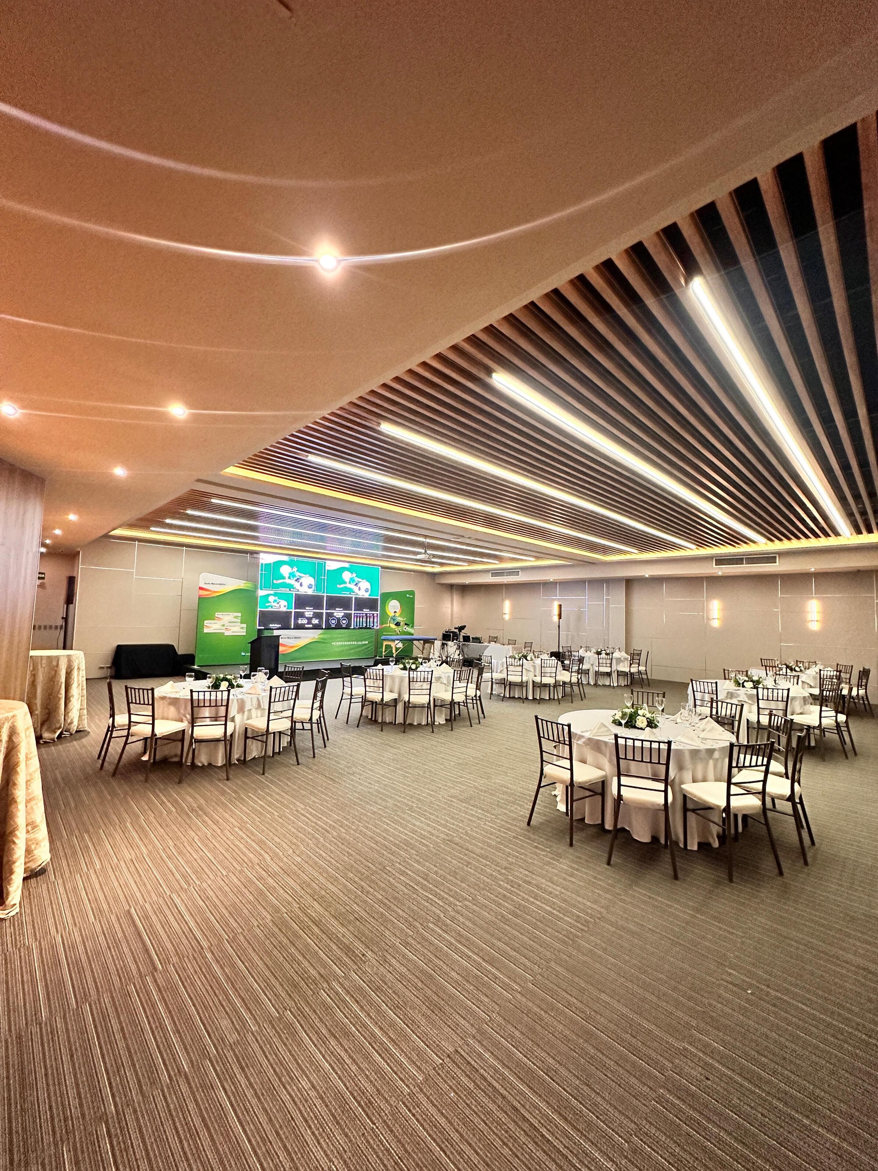 Uma sala de conferências com mesas redondas, cadeiras e uma tela grande para apresentações.