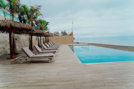 Una piscina al aire libre, sombrillas, sillones reclinables de piscina