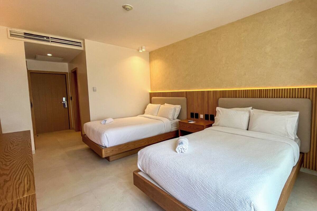 A hotel room with two beds, a wooden headboard, a bedside table, and a door leading to another room.