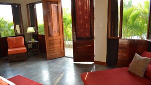 A room with a bed, a sofa, a small table with a lamp, and a view of palm trees through an open door. - Soma Surf Resort (Tola)