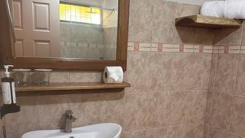 Uma casa de banho com uma pia branca, uma sanita, um espelho e uma estante com artigos de higiene pessoal.