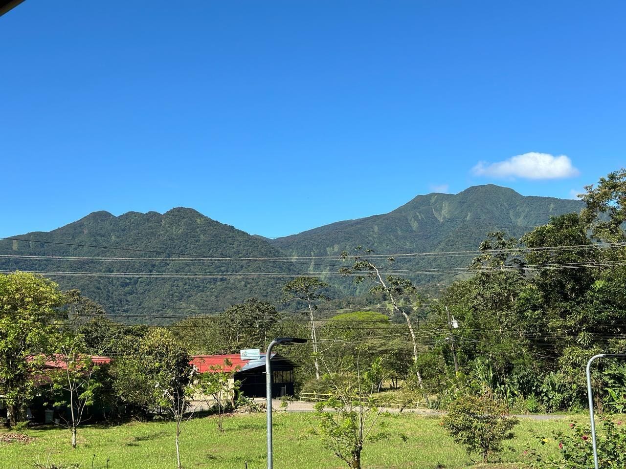 A rural landscape with a mountain range in the background, a small building with a red roof, and a clear blue sky.