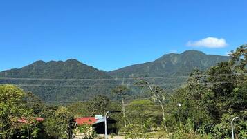 A rural landscape with a mountain range in the background, a small building with a red roof, and a clear blue sky.